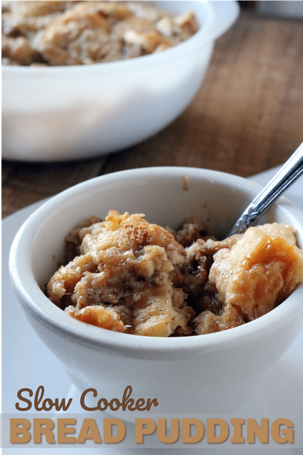 bread pudding in a bowl with a spoon in it on a plate with more bread pudding in another bowl in the background with title text reading Slow Cooker Bread Pudding