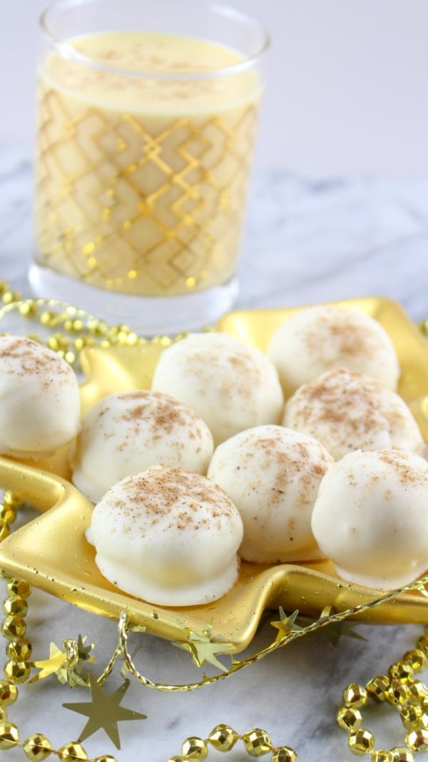 eggnog truffles on a gold Christmas tree plate with gold beads around it on a white counter with a glass of eggnog in the background
