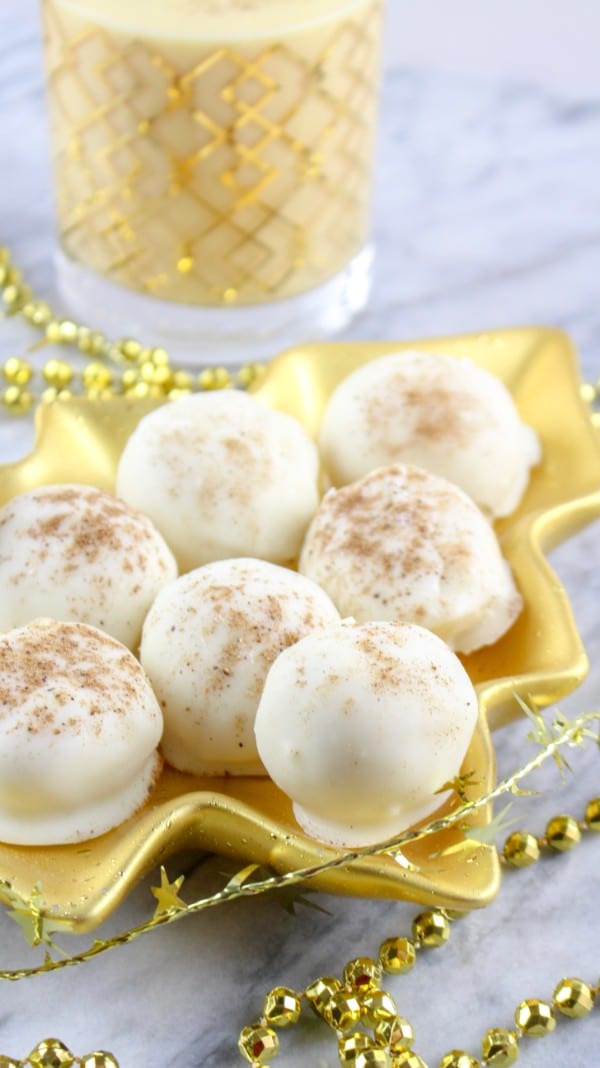 eggnog truffles on a gold Christmas tree plate with gold beads around it on a white counter with a glass of eggnog in the background
