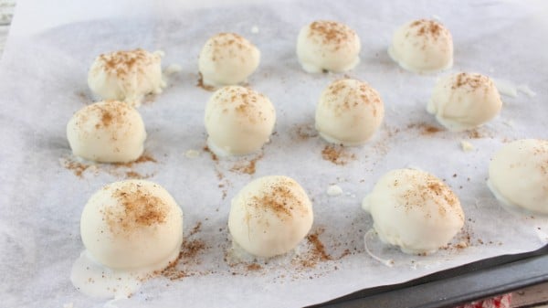 eggnog truffles dipped in white chocolate sprinkled with nutmeg on parchment paper on a cookie sheet