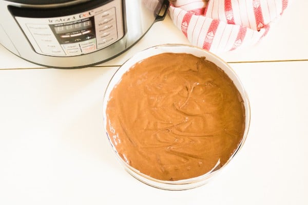 chocolate cheesecake batter in a paper lined springform pan with an instant pot and red and white cloth in the background, all on a white table