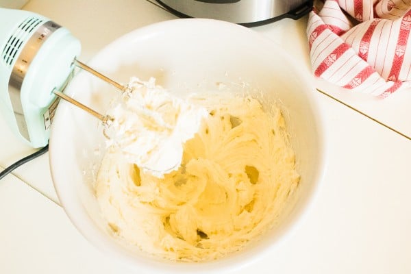 cream cheese and sugar in a white mixing bowl with a hand mixer in it