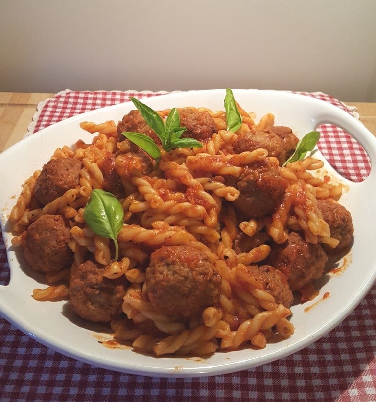 spaghetti and meatballs on a white plate on a red and white checkered cloth