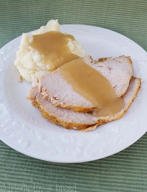 sliced turkey and mashed potatoes topped with gravy on a white plate on a green cloth
