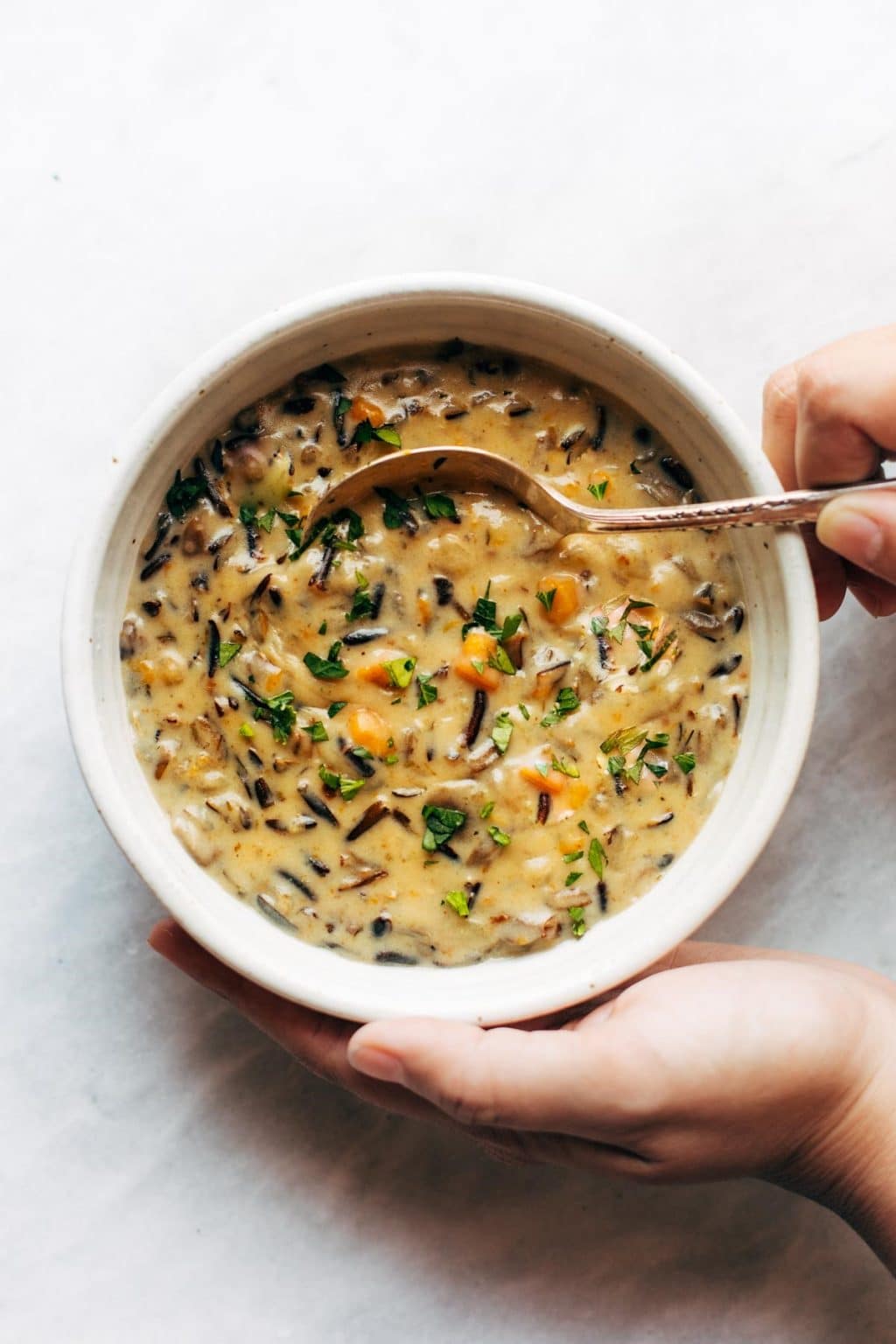 wild rice soup in a white bowl with a spoon in with hands holding the bowl