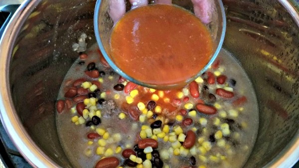 tomato juice being added to an instant pot with black beans, kidney beans, corn and ground beef in it