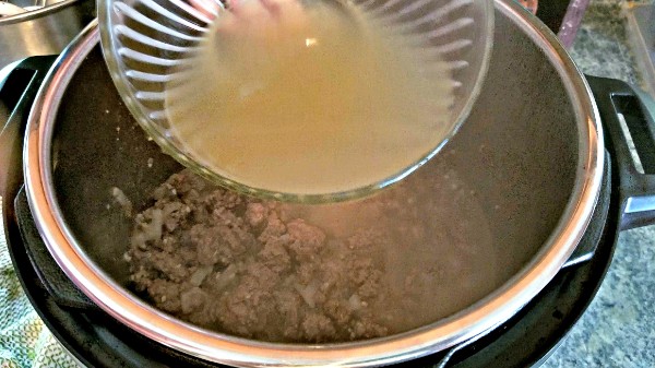 chicken broth from a glass bowl being poured into an instant pot of ground beef