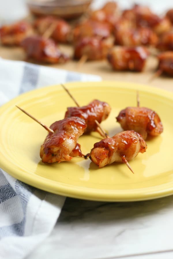 BBQ Bacon Wrapped Chicken Bites with toothpicks in them on a yellow plate with more in the background