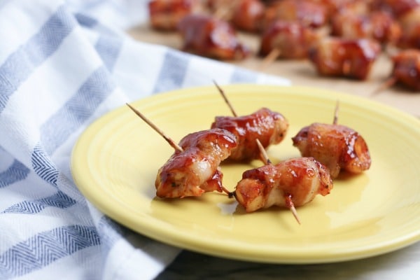 BBQ Bacon Wrapped Chicken Bites with toothpicks in them on a yellow plate with more in the background