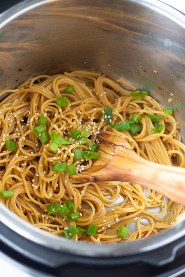 garlic noodles topped with sesame seeds and chopped green onions in an instant pot with a wooden spoon in it