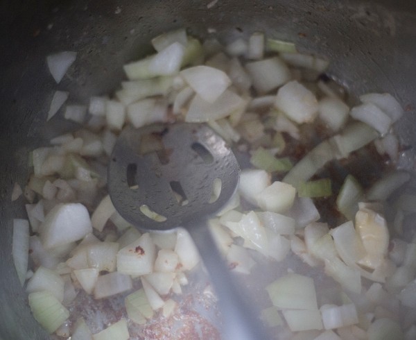 butter, onion, and garlic being cooked and stirred with a spoon in an instant pot