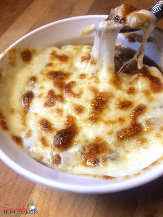 a bowl of french onion soup topped with cheese with a spoon scooping some up