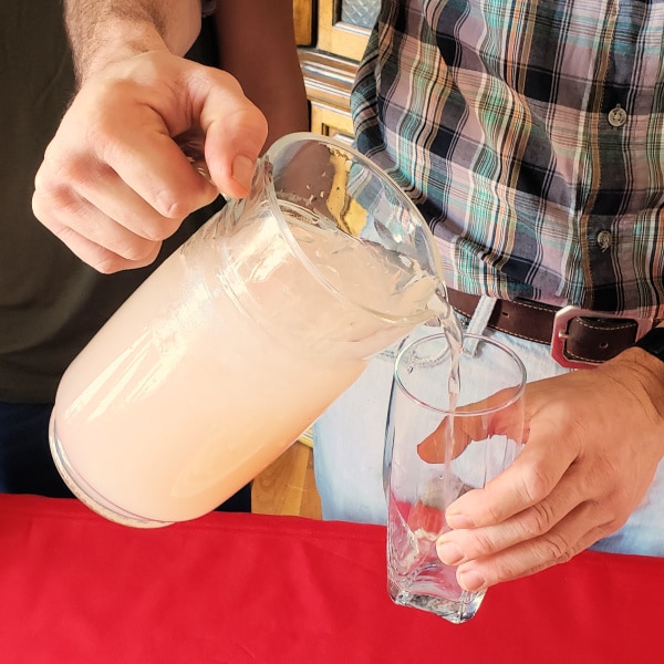 a man pouring lemonade from a glass pitcher into a glass 