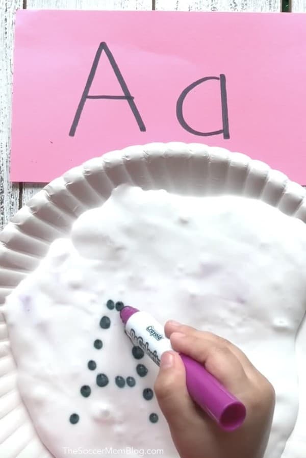 a plate of white foam with a child using a dot marker to make the letter A with a pink paper next to it with the letter A written on it