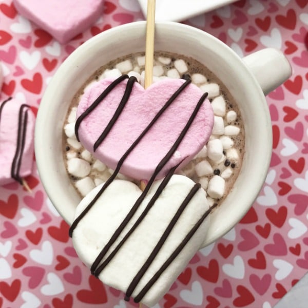 heart shaped marshmallows on wooden skewers on the top of a mug of hot cocoa topped with mini marshmallows