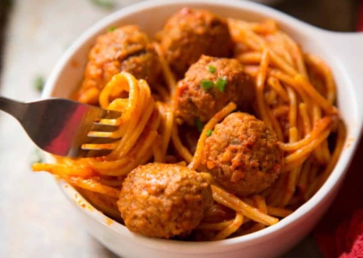 A white bowl of Spaghetti and Meatballs on a table with a fork in it.