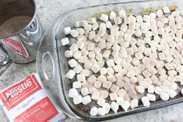 a sifter and envelope of hot cocoa next to a glass dish of cake topped with marshmallows
