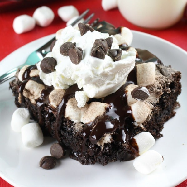 a slice of Hot Cocoa Chocolate Dump Cake topped with whipped cream and chocolate chips on a white plate with a fork next to it