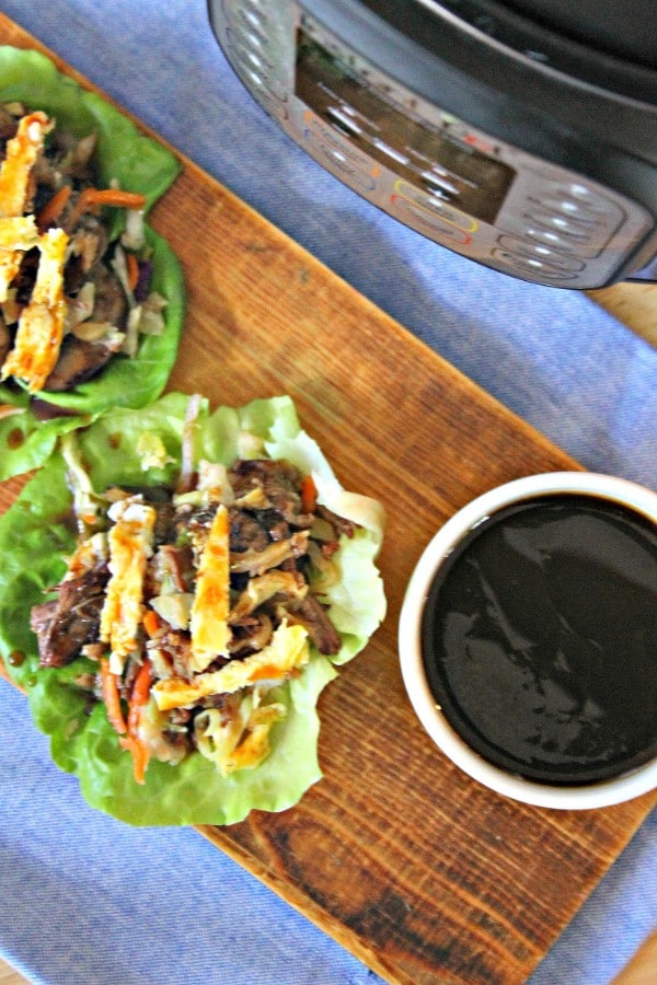 moo shu beef lettuce cups and a white bowl of sauce on a piece of wood on a blue linen with an instant pot in the background