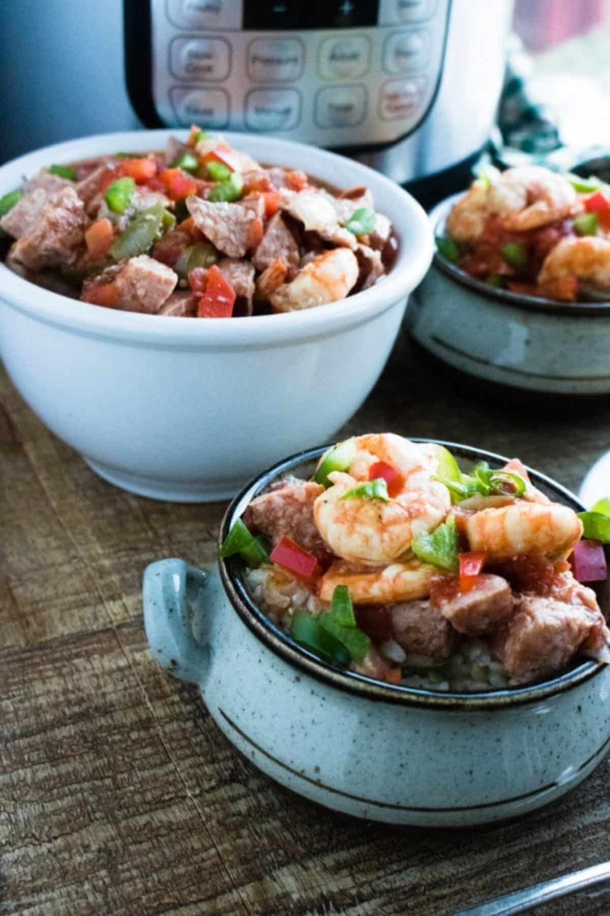 Three bowls filled with sausage & shrimp gumbo on a table with an instant pot in the background.
