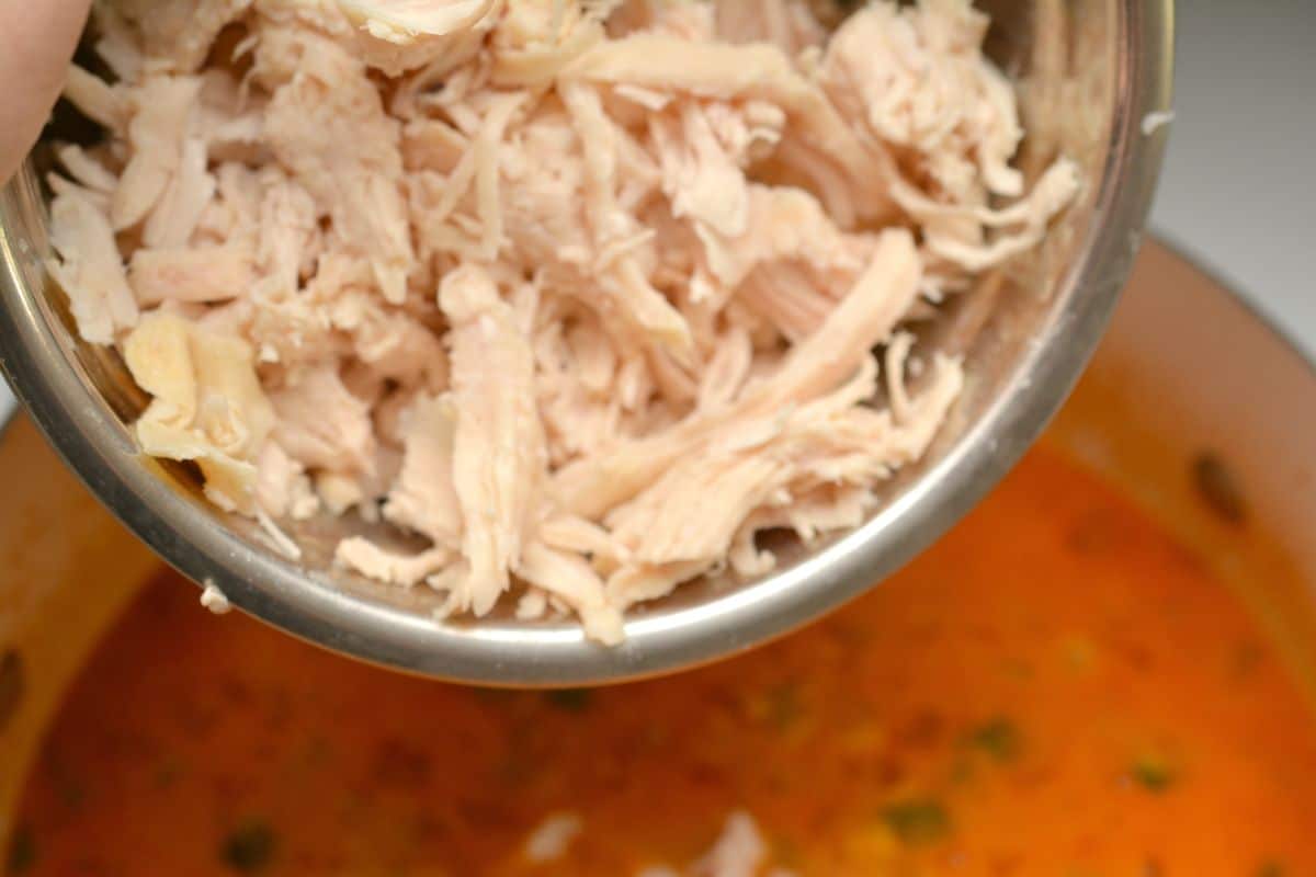 shredded chicken in a bowl being added to keto chicken enchilada soup.