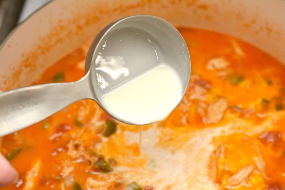 Adding heavy whipping cream from a measuring cup to keto chicken enchilada soup.