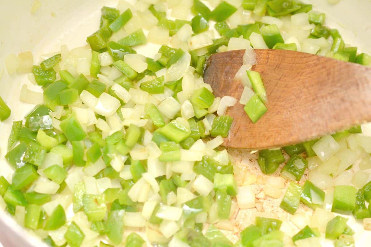 chopped onions and peppers in a pot with a wooden spoon.
