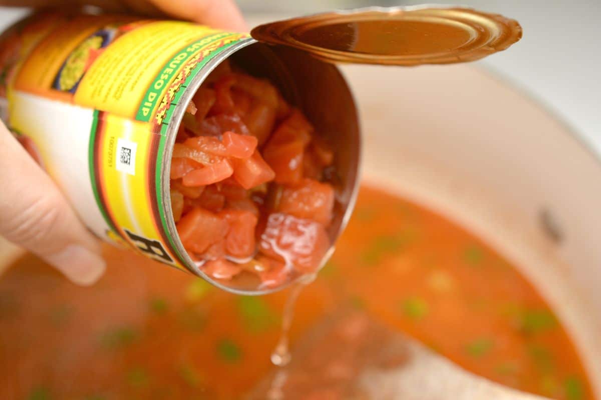 a can of diced tomatoes being poured into a pot.