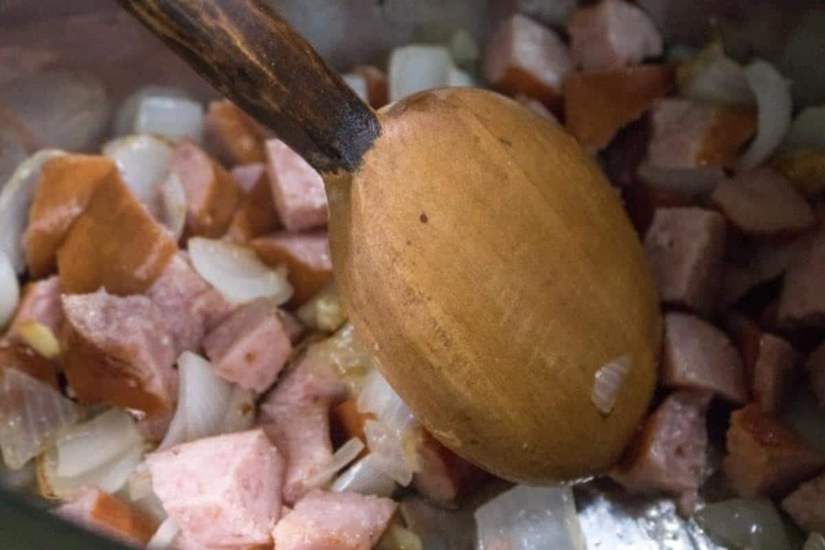 Sausage and onions and a wooden spoon in an instant pot.