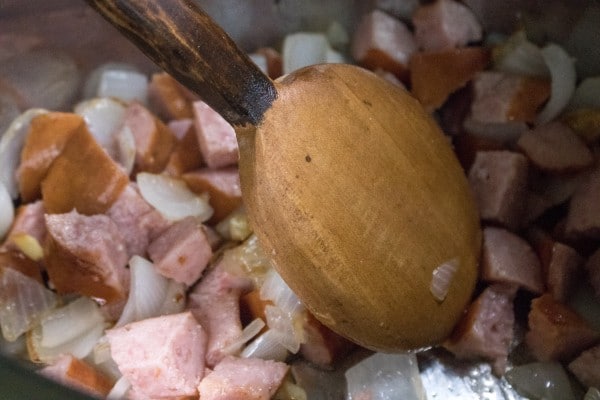 sausage and onions and a wooden spoon in an instant pot
