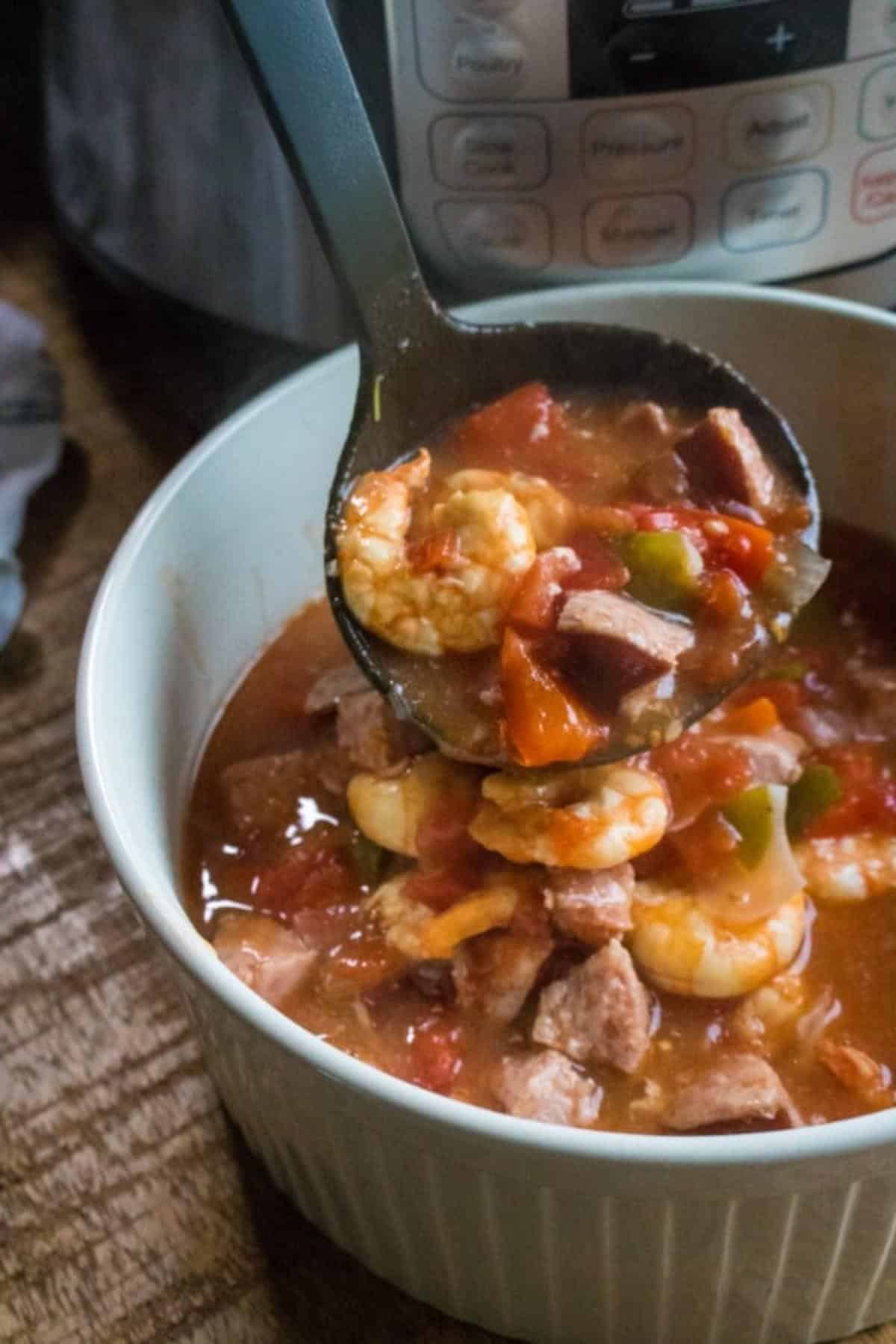 a spoonful of sausage and shrimp gumbo above a bowl of the gumbo on a table with an instant pot in the background.
