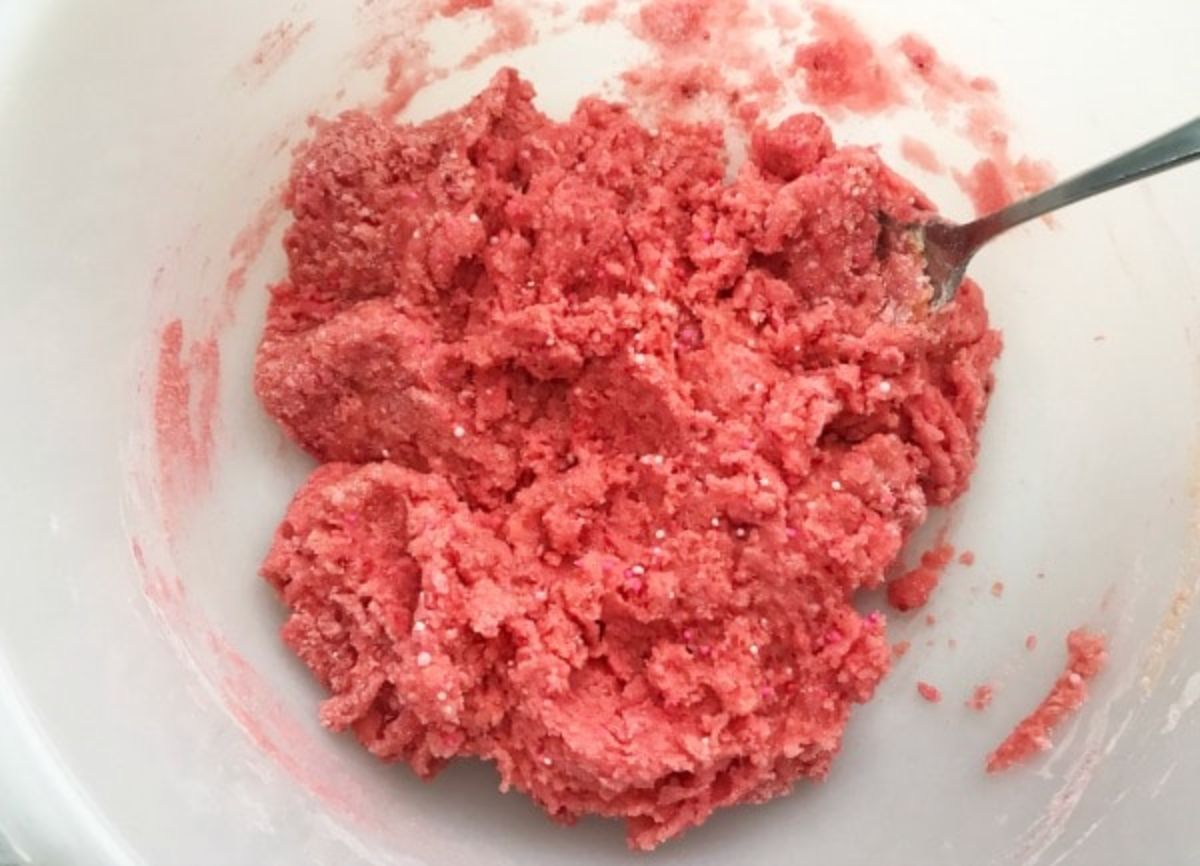 a utensil in the Strawberry Cake Mix Cookies batter in a white bowl.