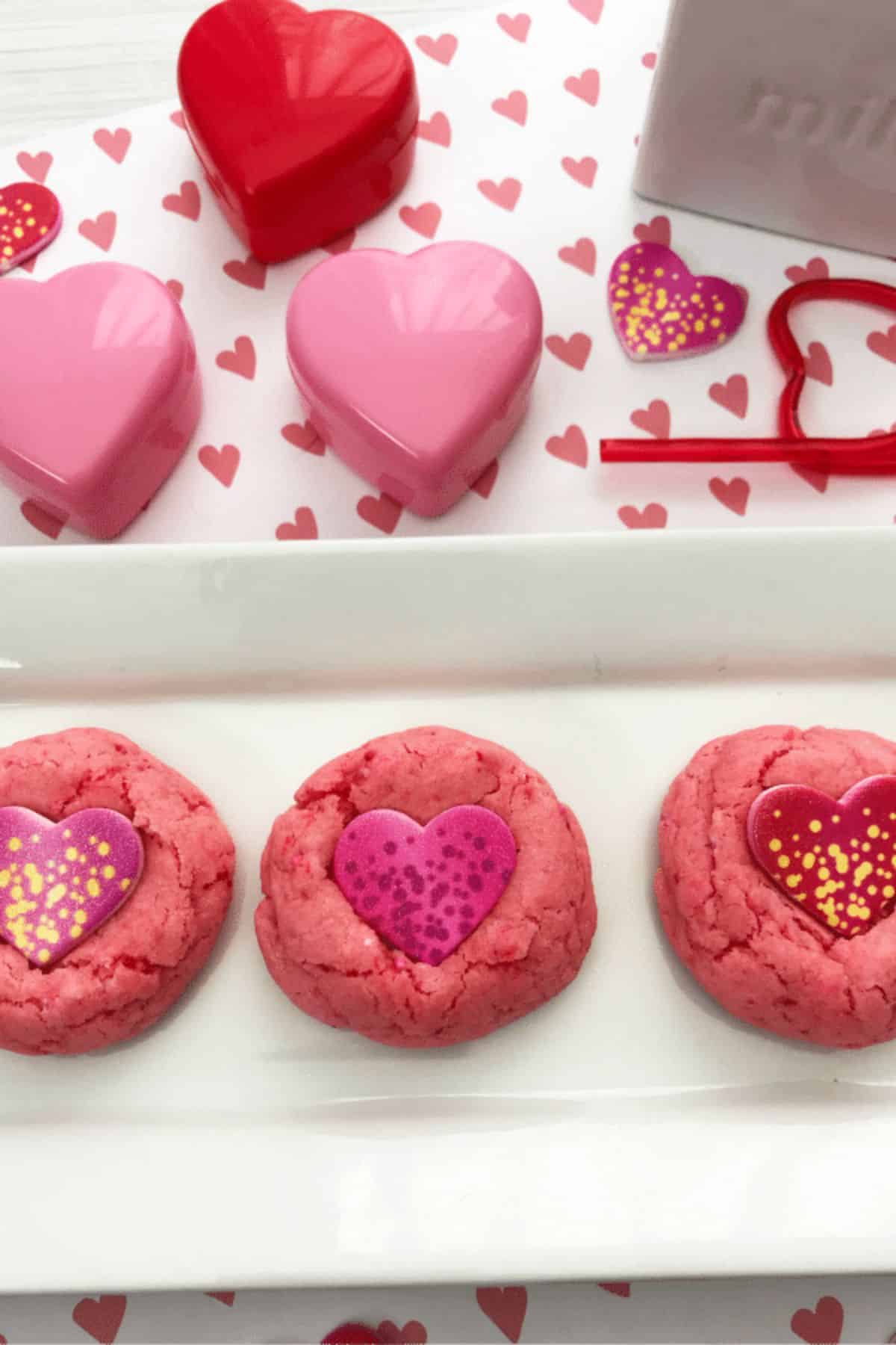 Strawberry Cake Mix Cookies on a tray on heart paper with plastic hearts and stickers next to it.