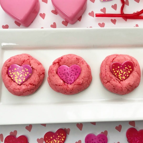 Strawberry Candy Heart Cookies on a tray on heart paper with plastic hearts and stickers next to it
