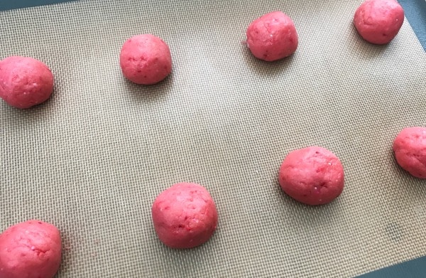 pink cookie dough in the shape of a ball on a baking mat