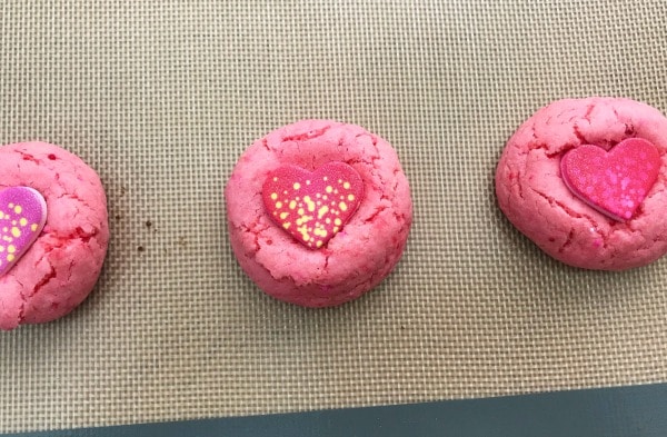 pink cookies with a candy heart pressed in them on a baking mat