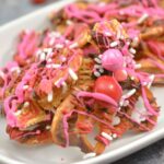 A plate of pretzels drizzled with pink and red icing, chocolate, and topped with sprinkles and candies creates a delightful Valentine Bark experience.