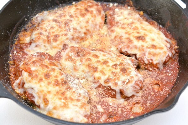 an oven skillet with chicken topped with sauce and cheese