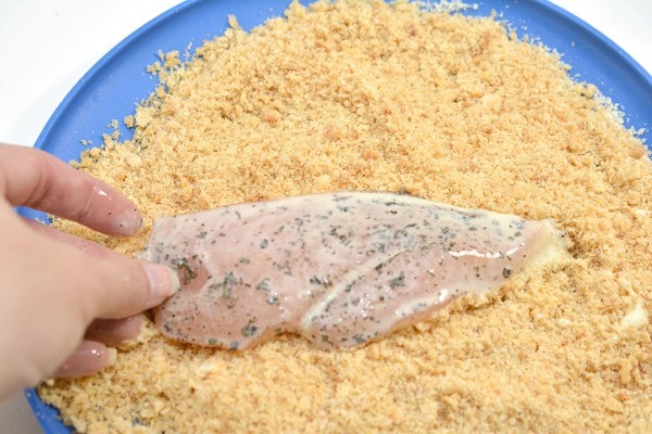 raw chicken breast being dipped in crumb mixture on a blue plate