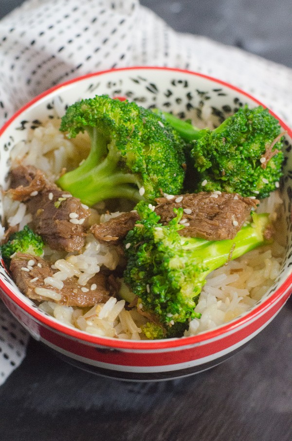  a bowl of beef, broccoli and rice on a table next to a cloth