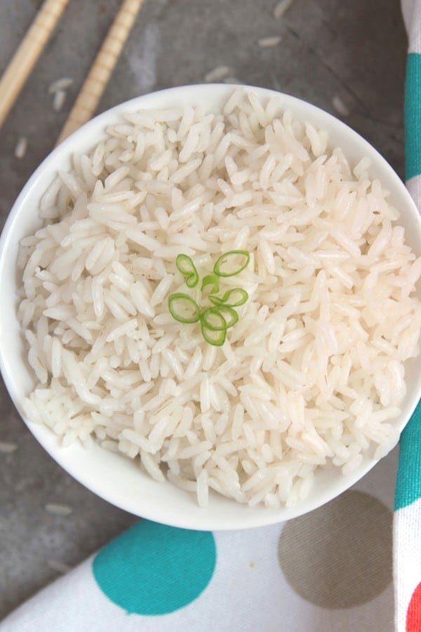 white rice in a white bowl topped with green onions next to chopsticks and a polka dot cloth