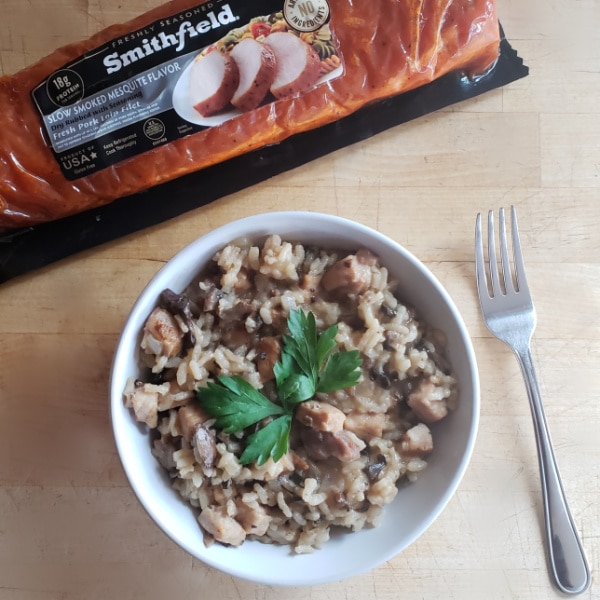 pork risotto in a white bowl next to a fork, with a package of pork in the backgorund