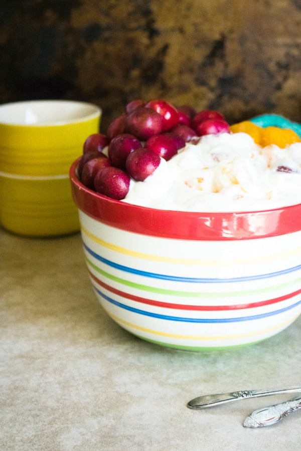 Pudding Fruit Salad in a multi-colored striped bowl with 2 more bowls in the background