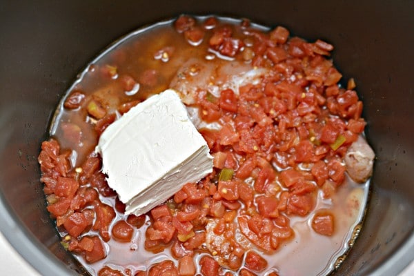 an instant pot filled with chicken, diced tomatoes, and liquid topped with a block of cream cheese