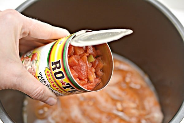 a hand holding a can of diced tomatoes over and instant pot with chicken and sauce in it