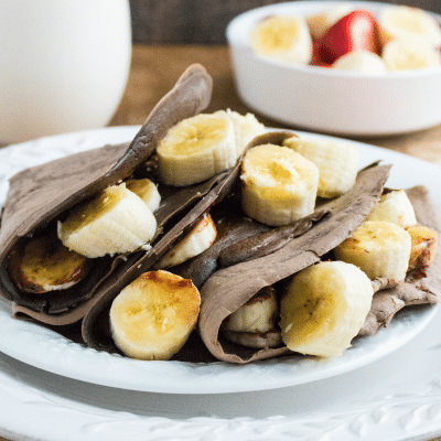 Chocolate Nutella and Banana Crepes on white plate with cup of milk in background