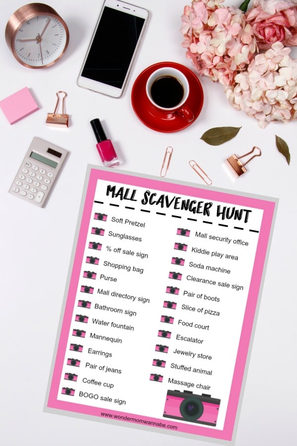 printable Mall Scavenger Hunt list on a white table next to a clock, cell phone, calculator, sticky notes, paper clips, a cup of coffee and flowers