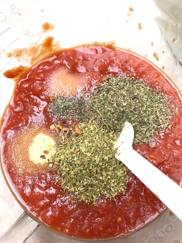 crushed tomatoes and spices being stirred with a white spoon in a bowl