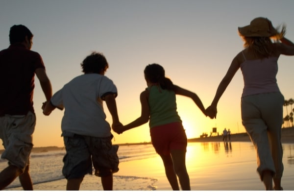 a family holding hands running on a beach at sunset