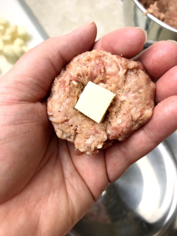 a hand holding a raw meatball with a square of mozzarella in the middle
